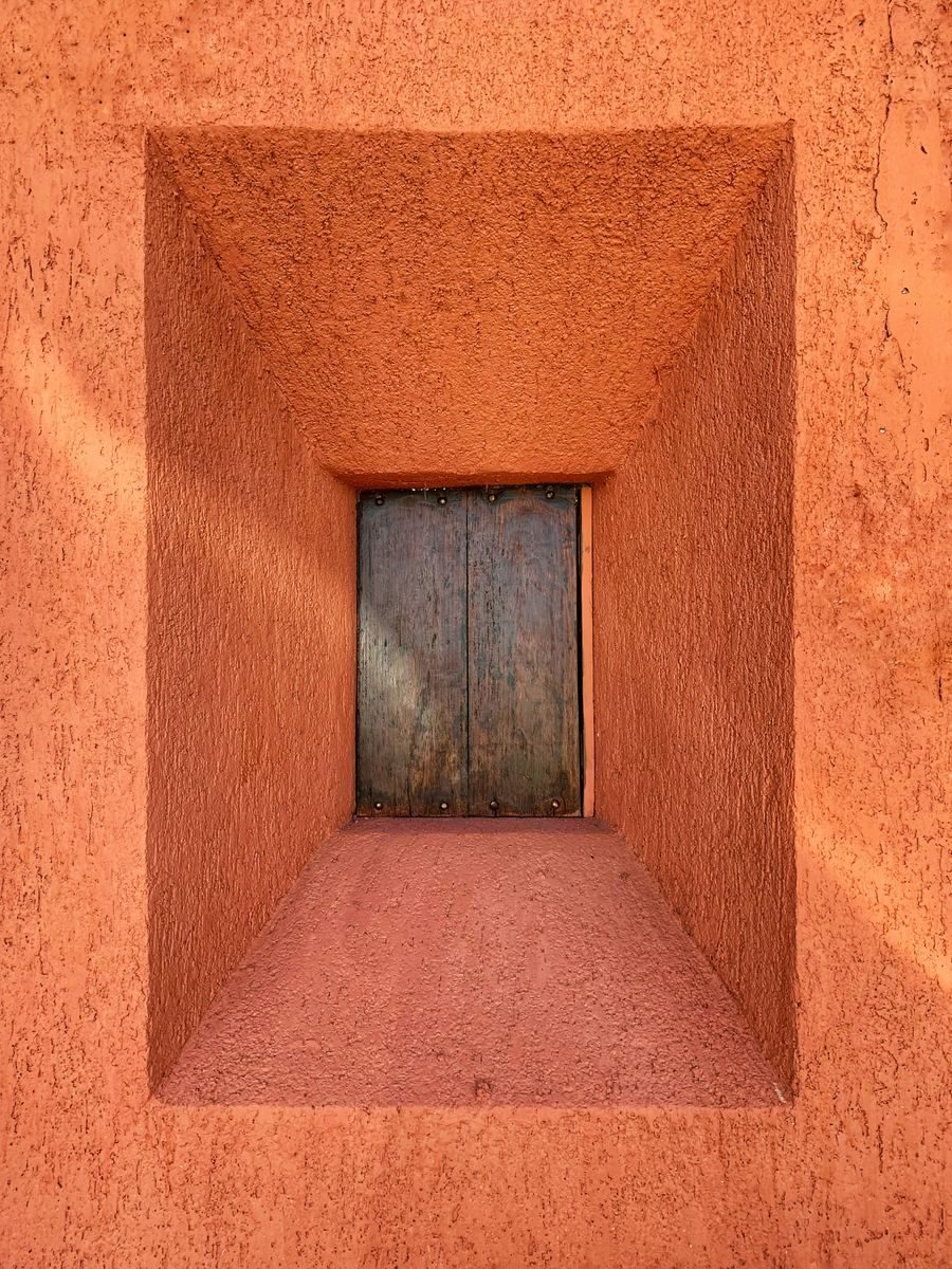 A terracotta doorway looking down a short corridor to a timber door.