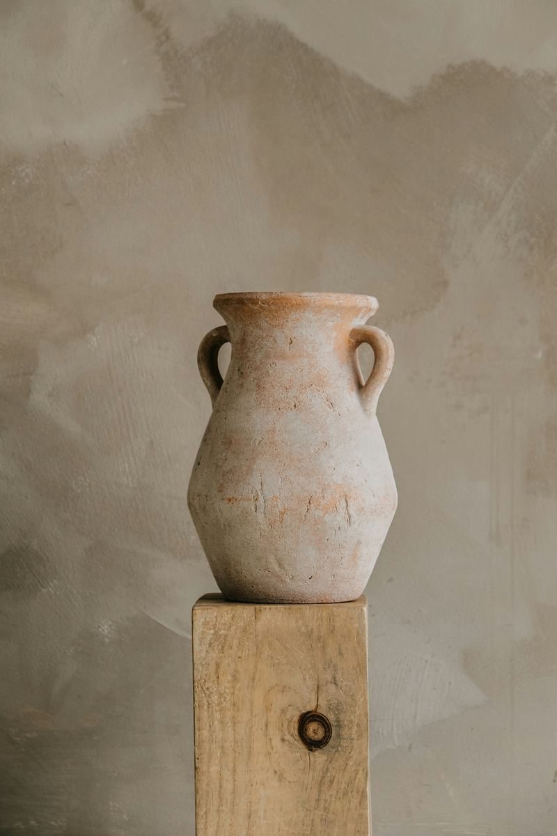 A terracotta vessel standing on a timber plinth against a plastered wall.